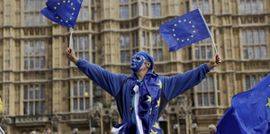 Ein in EU-Farben gekleideter Mann mit zwei EU-Fahnen in der Hand