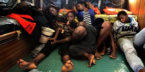 Mehrere junge Menschen liegen erschöpft auf dem Deck eines Schiffes