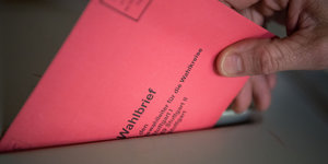 Eine Hand steckt einen roten Briefumschlag in eine Wahlurne