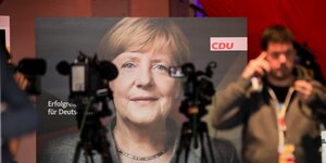 Ein Plakat mit Merkels Konterfei vor Kameras