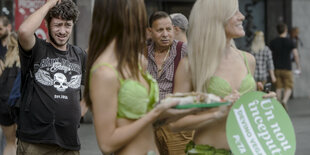 Frauen tragen Bikinis aus Salat und tragen Peta-Werbung, ein Mann kuckt skeptisch und kratzt sich am Kopf