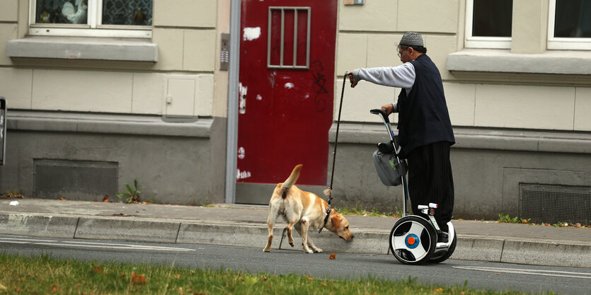 Ein Mann auf einem Segway, daneben ein Hund, den er an der Leine hält