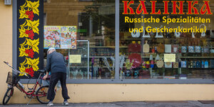 Ein Mann bückt sich über ein Fahrrad, das vor einem russischen Lebensmittelgeschäft steht