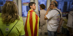 Mehrere Menschen in einer fahrenden U-Bahn. Ein Junge hat wie einen Umhang eine katalonische Flagge um.