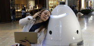 Eine Frau mit einem Laptop in der Hand lehnt sich an einen Roboter
