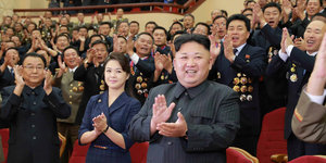 Kim Jong Un steht mit vielen Menschen in einem Saal