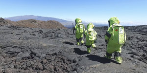 Menschen in Raumanzügen laufen auf Vulkangestein