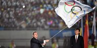 Ein Mann schwenkt eine große Flagge mit dem Olympischen Zeichen der fünf verschiedenfarbigen Ringe
