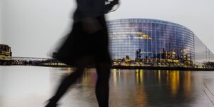 Die Silhouette einer Frau, die vor einem Bild des Europaparlaments vorbeiläuft