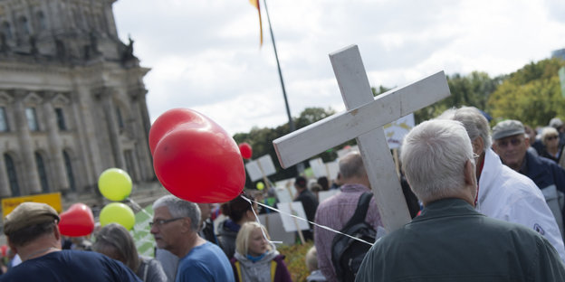 Menschen mit Luftballons. Einer trägt ein weißes Kreuz