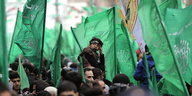 Eine Menschenmenge hält große, grüne Flaggen hoch. Mittendrin sitzt eine Junge auf den Schultern eines Mannes