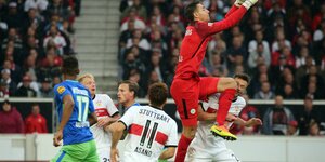 Eine Szene aus einem Fußballspiel: Ein Mann in rotem Trikot springt hoch und streckt seine Hände hoch, dabei trifft sein Knie einen Mann in weißem Trikot im Gesicht