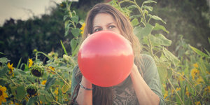 Eine Frau in einem Garten bläst einen roten Luftballon auf