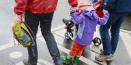 Ein Kind in einer lila Regenjacke wird an beiden Händen von Erwachsenen gehalten und hüpft
