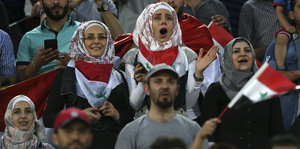 Frauen mit Kopftüchern inmitten einer jubelnden Menge auf der Tribüne eines Fußballstadions