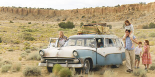 Familie in karger Landschaft neben altem Kombi