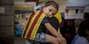 Ein Mädchen sitzt auf der Schulter eines Erwachsenen, die Flagge Kataloniens auf dem Rücken tragend