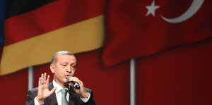 Erdogan sprich in ein Mikrofon, er steht vor einer Deutschland- und einer Türkei-Flagge