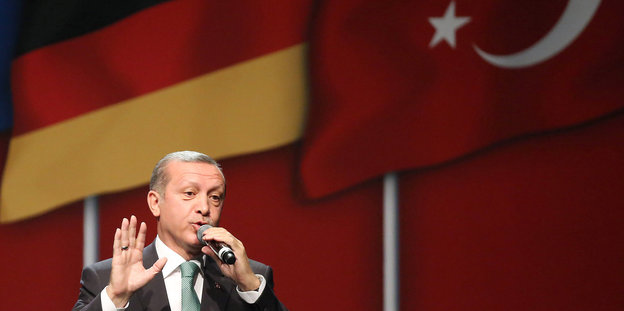 Erdogan sprich in ein Mikrofon, er steht vor einer Deutschland- und einer Türkei-Flagge