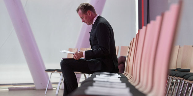 Ein Mann sitzt in einer leeren Stuhlreihe und sortiert Papier