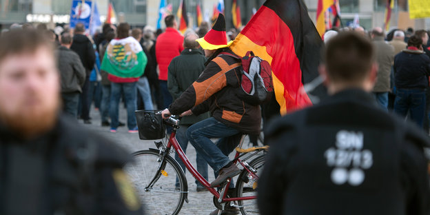 Ein Mann mit Deutschlandfahne fährt durch eine Menschenmenge