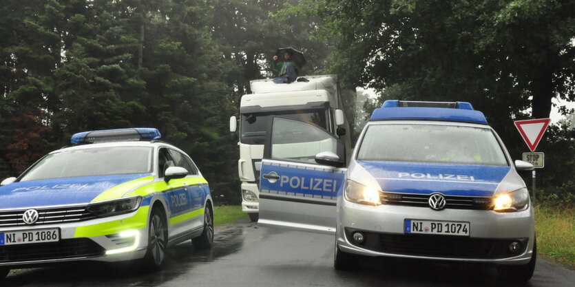 Ein Mann sitzt auf einem LKW und hindert diesen so daran weiterzufahren. Davor ist Polizei zu sehen