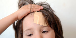 Ein Kind hat ein Pflaster an der Stirn und fässt sich an den Kopf