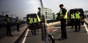 Polizisten in Warnwesten stehen auf einer Straße und kontrollieren Autos