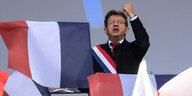 Ein Mann spricht und reckt eine Faust in die Höhe, vor ihm sieht man Frankreichflaggen