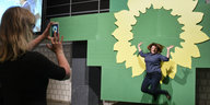 Wahlparty der Grünen: Eine Frau fotografiert eine andere Frau, die vor der Sonnenblume der Grünen in die Luft springt.
