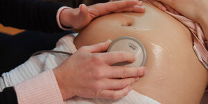 Ein Bauch einer schwangeren Person, auf dem ein medizinisches Gerät (Ultraschall) liegt