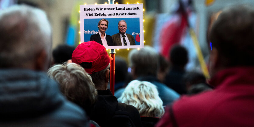 Ein Schild mit "Holen wir unser Land zurück. Viel Erfolg und Kraft dazu" und einem Bild der AfD-Spitzenkandidat*innen ragt aus einer Menschenmasse