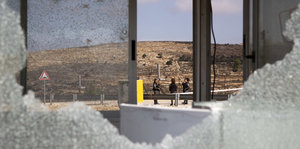 Eine zersplitterte Glasscheibe, dahinter ist der Checkpoint und Soldaten zu sehen