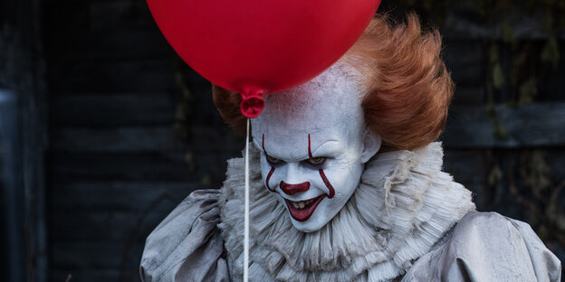 Ein Clown lacht böse. Vor seiner Stirn ist ein Luftballon