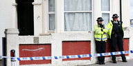 Zwei britische Polizisten stehen an eine Hausmauer links im Bild gelehnt