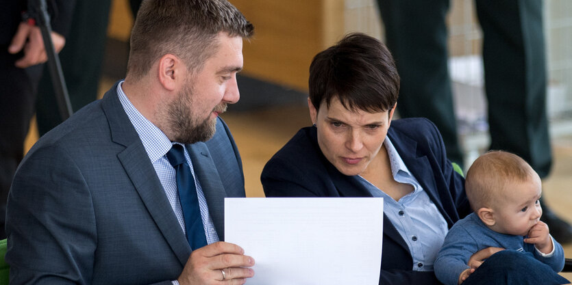 Frauke Petry lehnt sich weit nach rechts um ihrem Sitznachbar in die Notizen gucken zu können, auf dem Schoß hält sie ihr Baby