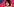 Eine Frau sitzt vor einem pinkfarbenen Hintergrund, spricht in ein Mikro und hat eine Faust geballt