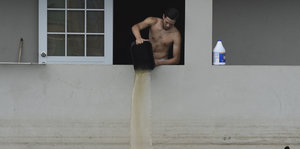 Ein Mann steht am Fenster und kippt ein Eimer mit Wasser aus