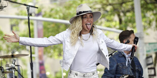 Miley Cyrus trägt einen Hut, streckt die Zunge raus und breitet die Arme aus