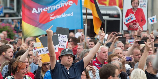 Eine Menschenmenge mit AfD-Transparent, einige Menschen zeigen den Mittelfinger