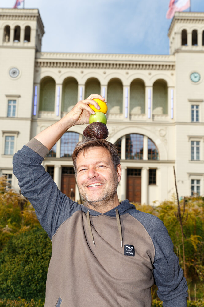 Robert Habeck stapelt Avocado, Zitrone und Apfel auf seinem Kopf