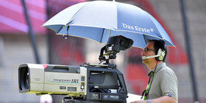 Ein Kameramann, geschützt von einem Schirm mit ARD-Logo