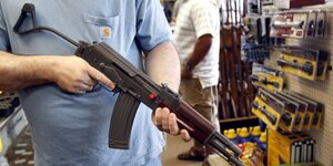 Eine Person hält ein Gewehr in einem Waffenladen
