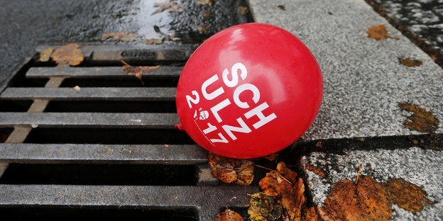 Ein roter Ballon mit der Aufschrift Schulz 2017 liegt auf einem Gulli
