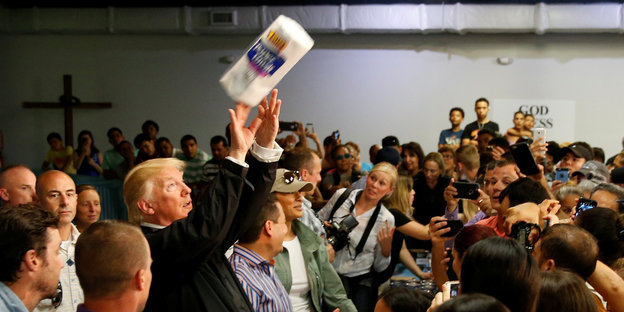Donald Trump wirft eine Papierrolle in eine Menschenmenge