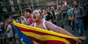 Eine Frau hält die Fahne Kataloniens in den Händen und schreit. Hinter hier ist eine Menschenmenge zu sehen