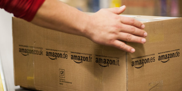 Hände greifen eine Pappbox, auf der Amazon steht