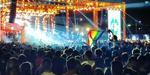 Menschenansammlung vor einer Bühne mit Regenbogenfahne