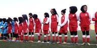 Mehrere Mädchenin in Trikots und Kopftüchern stehen auf einem Fußballfeld in einer Reihe nebeneinander