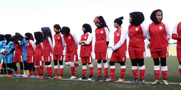 Mehrere Mädchenin in Trikots und Kopftüchern stehen auf einem Fußballfeld in einer Reihe nebeneinander